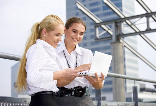 two happy businesswomen with laptop computer in the city (focus on blonde)