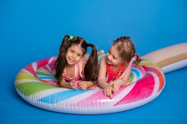 Two happy child girl in swimming suit lying on colorful inflatable mattress lollipop