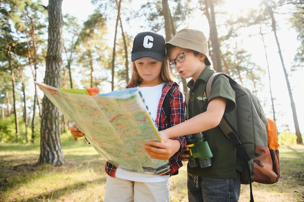 Two happy children having fun during forest hike on beautiful\
day in pine forest cute boy scout with binoculars during hiking in\
summer forest concepts of adventure scouting and hiking\
tourism
