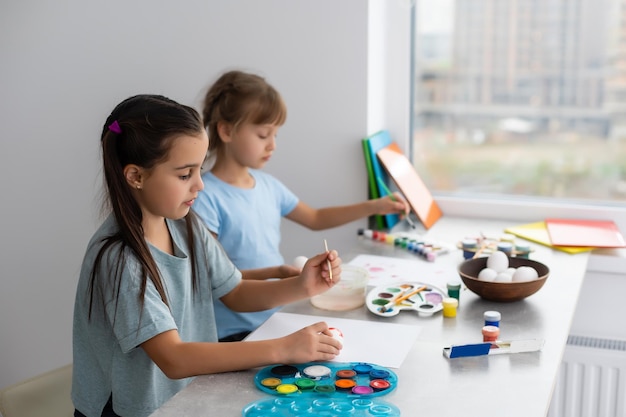 two happy cute girls sisters paint easter eggs, oh laugh, show eggs and painted hands