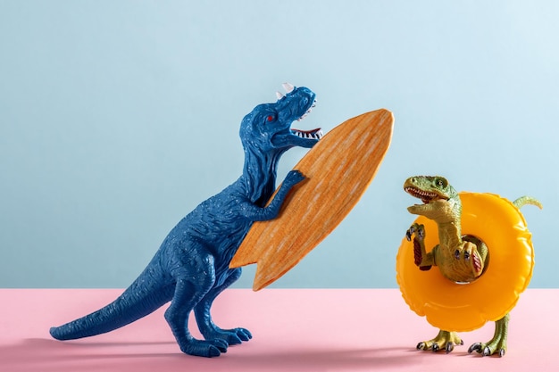 Photo two happy dinosaurs with surfboard and an inflatable circle on pink and blue background