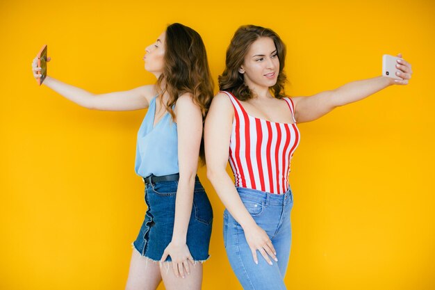 Two happy elegant women in dresses posing together and making selfie on smartphone