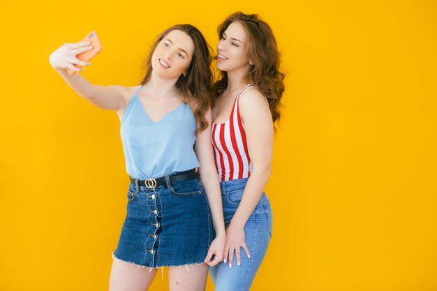 Two happy elegant women in dresses posing together and making selfie