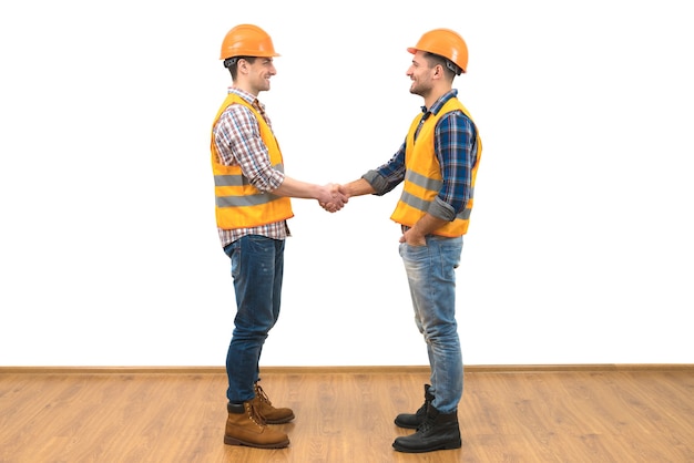 The two happy engineers handshake on the white wall background