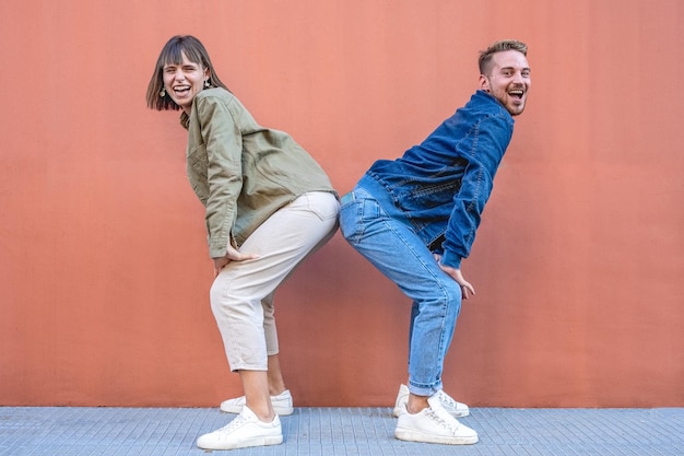 Two happy excited stylish diverse gen z woman and man friends
dancing and having fun trendy outfits people dancing together
isolated on pink wall backgroung generation z lifestyle