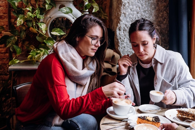 Two happy female friends talk and catch up in a modern coffee during winter