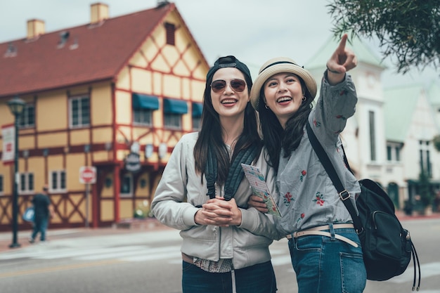 Two happy friends holding map pointing outdoors