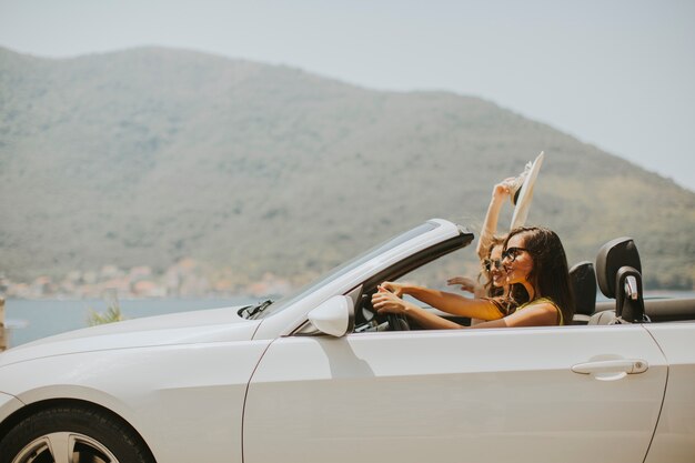 Two happy friends in white cabriolet car driving and looking for freedom and fun