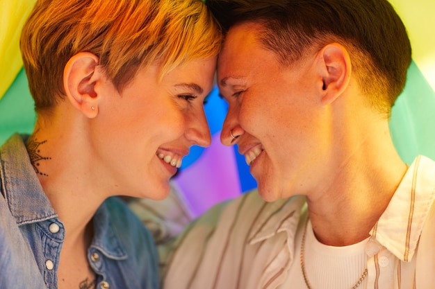 Two happy girlfriends looking at each other and smiling under the colored flag