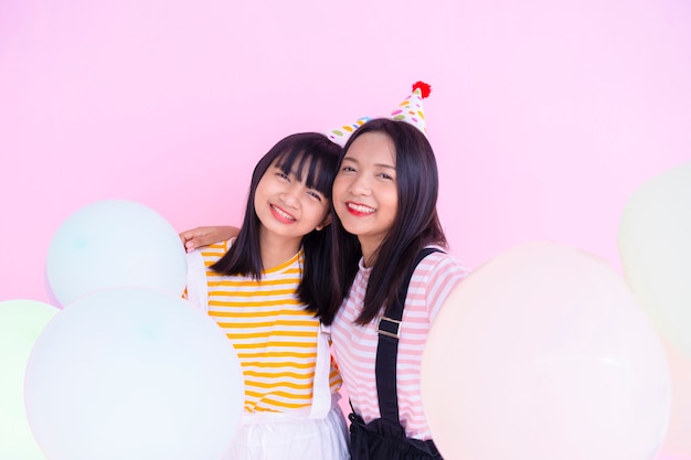 Two happy girls hold balloon on pink background.