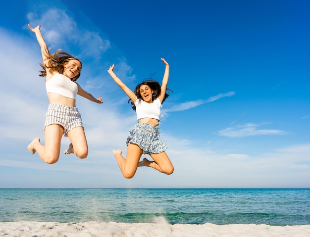 two happy girls jumping together on tropical beach enjoying summer vacation