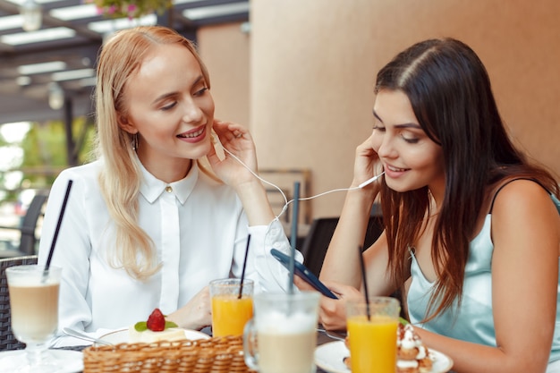 Two happy girls listening to music with shared earphones together in nice cafe. Enjoy music and entertainment