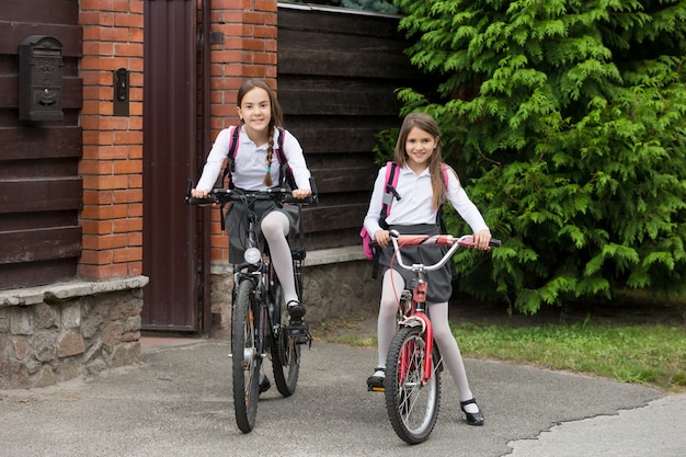 Due ragazze felici in uniforme scolastica che vanno a scuola in bicicletta