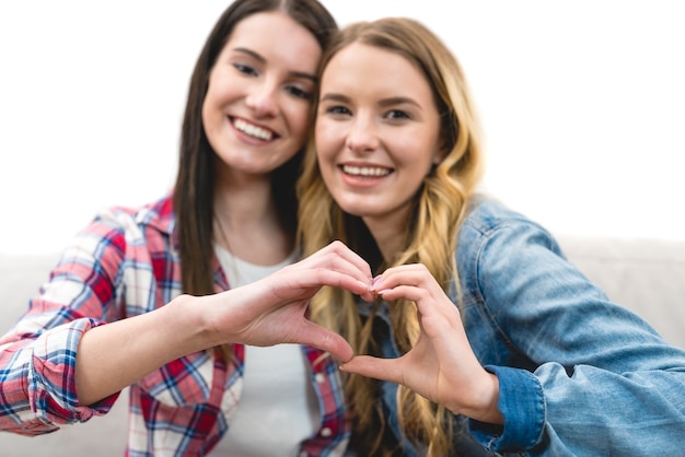 The two happy girls show the heart symbol on the white background