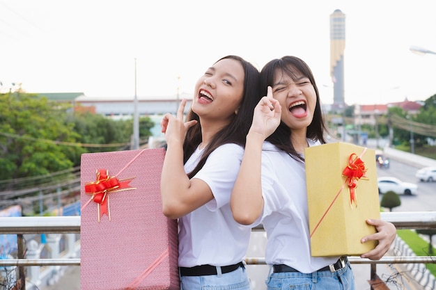 Two happy girls with gift boxes standing with city background.