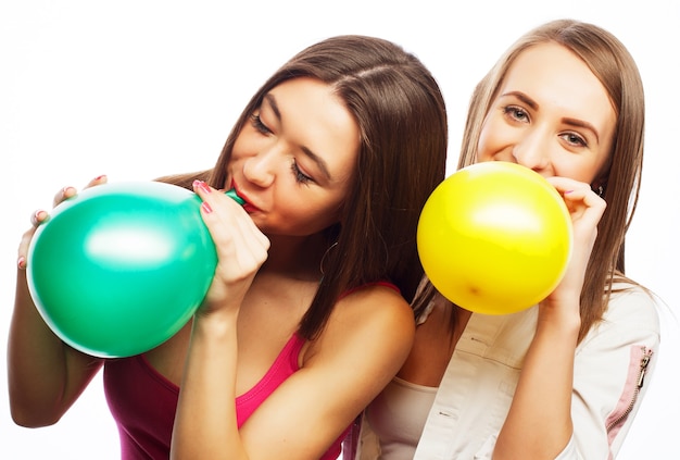 Two happy hipster girls smiling and holding colored balloons over white background