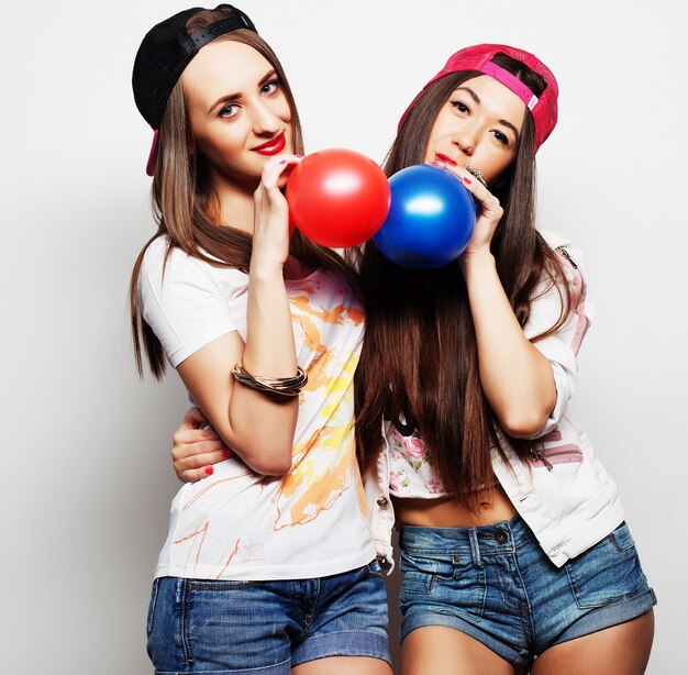 Two happy hipster girls smiling and holding colored balloons over white background