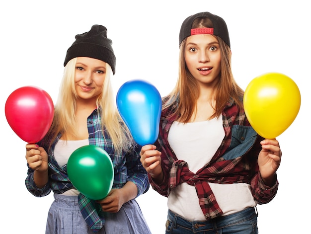 Two happy hipster girls smiling and holding colored balloons over white background