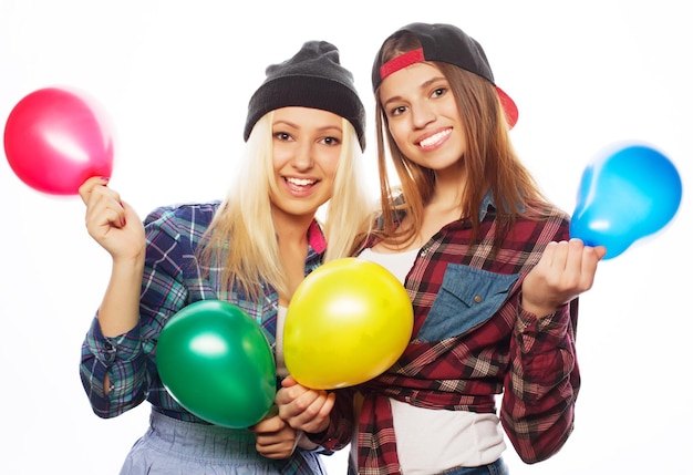 Two happy hipster girls smiling and holding colored balloons over white background