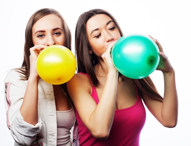 Two happy hipster girls smiling and holding colored balloons over white background