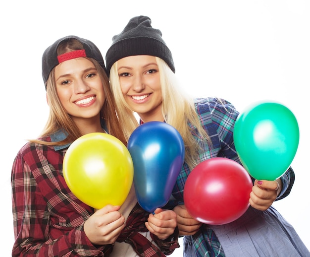 Two happy hipster girls smiling and holding colored balloons over white background