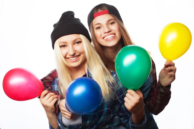 Two happy hipster girls smiling and holding colored balloons over white background