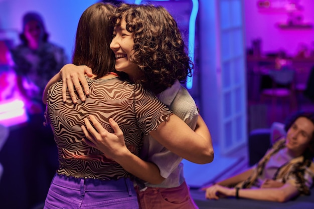 Two happy intercultural girls standing in embrace at party