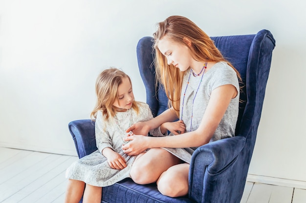 Two happy kids sitting on cozy blue chair relaxing playing in white living room at home