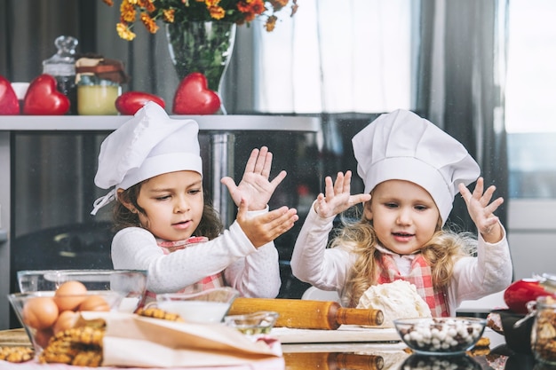 Two happy little girls child cook with flour and dough at the table in the kitchen is lovely and beautiful