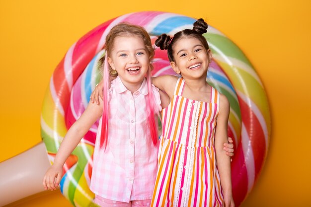 Two happy little girls in colorful dress laughing hugging having fun with lollipop.