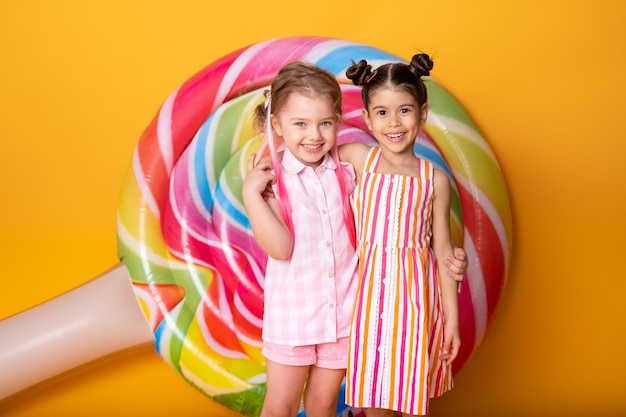 Two happy little girls in colorful dress laughing hugging having fun on yellow surface.