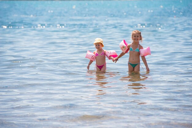 여름 방학 동안 바다의 얕은 물에서 수영 완장을 가진 두 명의 행복한 어린 소녀 건강한 어린 시절 생활 방식 개념