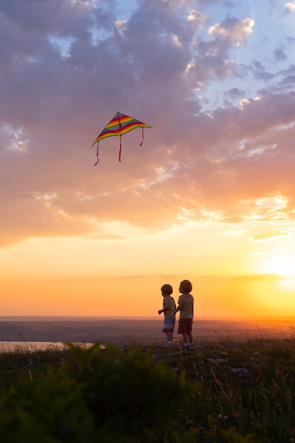 Due ragazzini felici che si divertono con l'aquilone in natura al tramonto