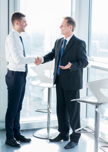 Two happy male business partners shaking hands in office