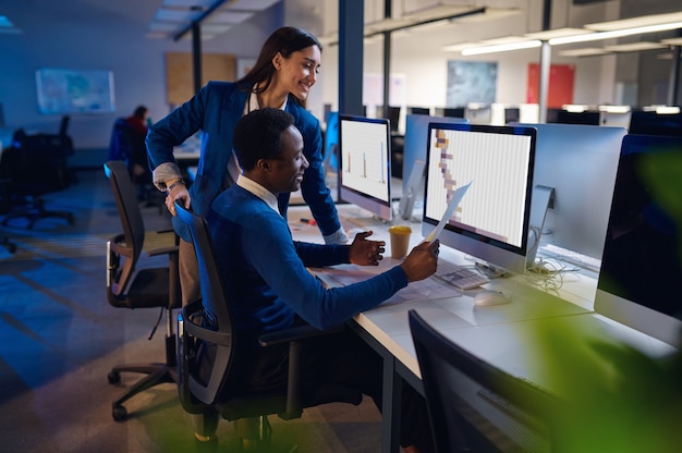 Two happy managers working in night office. Male and female workers, dark business center interior, modern workplace