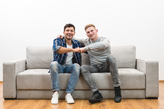 The two happy men on the sofa gesture on the white wall background