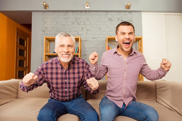 Two happy men watching football at home with raised hands