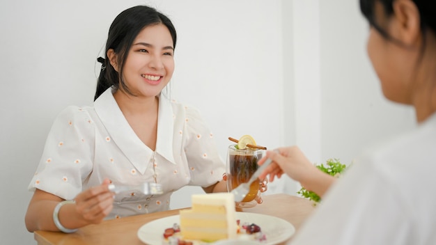 Two happy millennial Asian women friends enjoy eating dessert and chatting in the cafe together