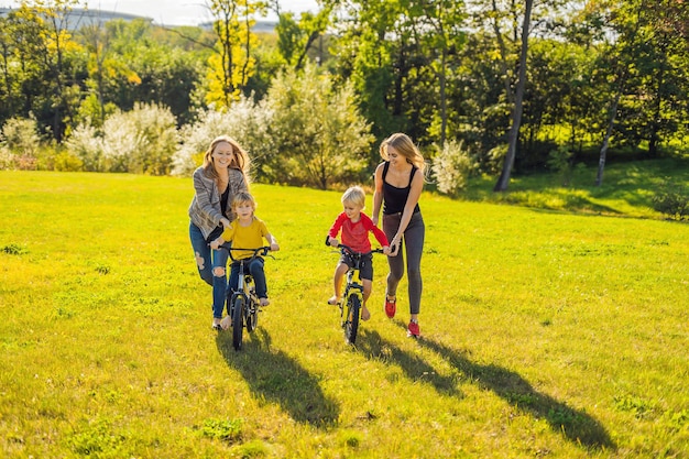 Two happy mothers teach their happy sons to ride a bike.