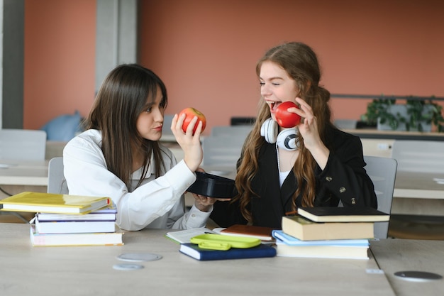 2人の幸せな笑顔の女子学生が座ってリンゴを食べて勉強し、試験の準備をしている