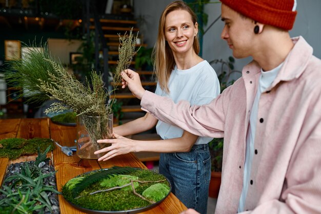 Two happy and smiling florists working together at creative workshop studio. Young man and woman making beautiful home decoration for design interior