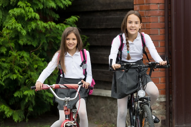 Two happy smiling girls in uniform riding to school on bicycles