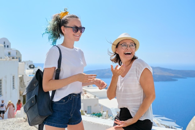 Two happy smiling women, mother and teenage daughter traveling together, luxury travel to the famous greek island of Santorini