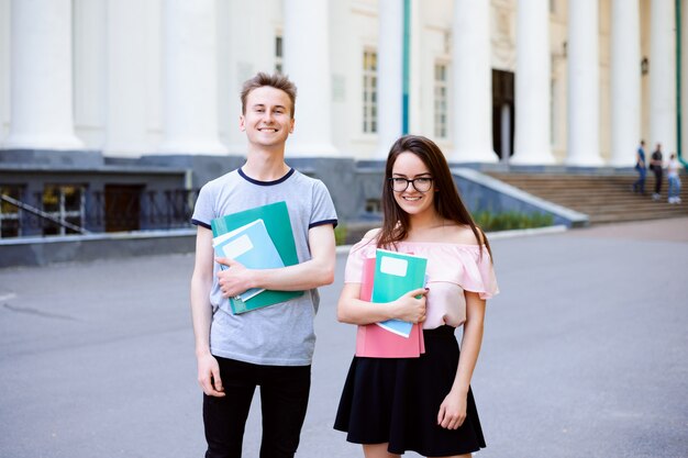 2 счастливых студента перед университетом с книгами и тетрадями