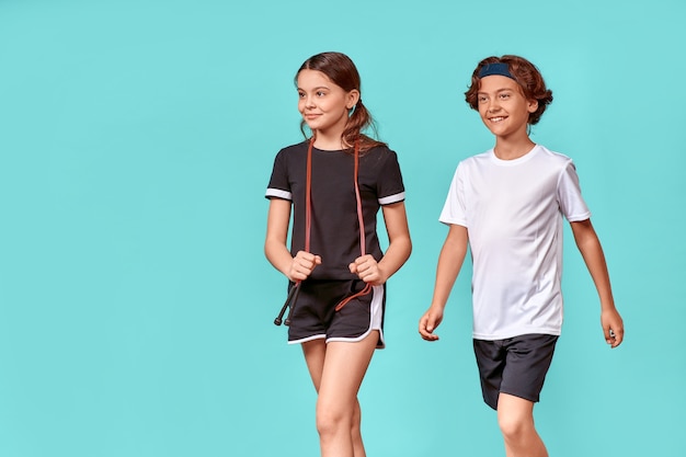 Two happy teenagers boy and girl with jumping rope looking away and smiling while standing isolated