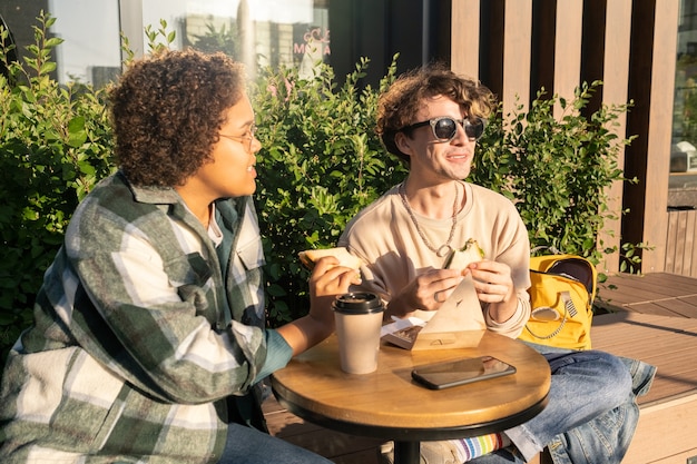 Two happy teenagers having snack and drinking coffee outside