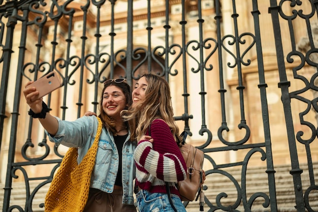 Photo two happy tourist friends take a selfie in front of the cathedral of malaga