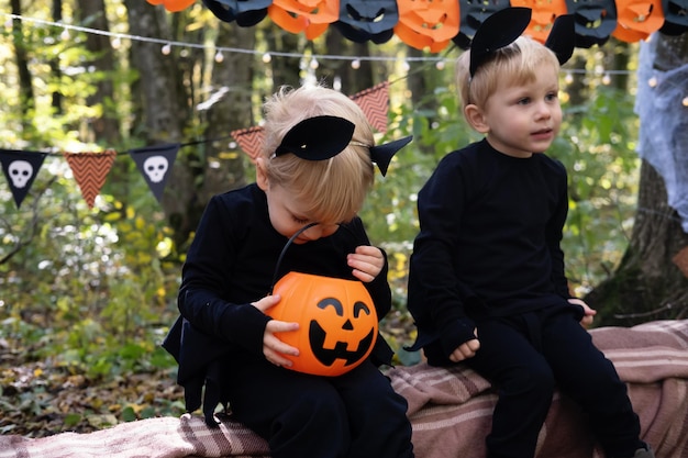 屋外のハロウィーンの装飾で楽しんでいるハロウィーンの衣装で 2 つの幸せな双子の男の子の子供