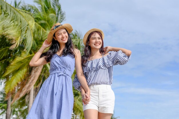 Two happy woman holding straw hat at the beach with coconut trees