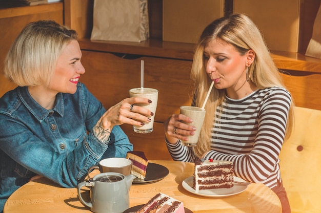 Two happy women sitting in a cafe, drink a cocktail, tell each other funny stories, being in a good mood, laughing happily. Best friends